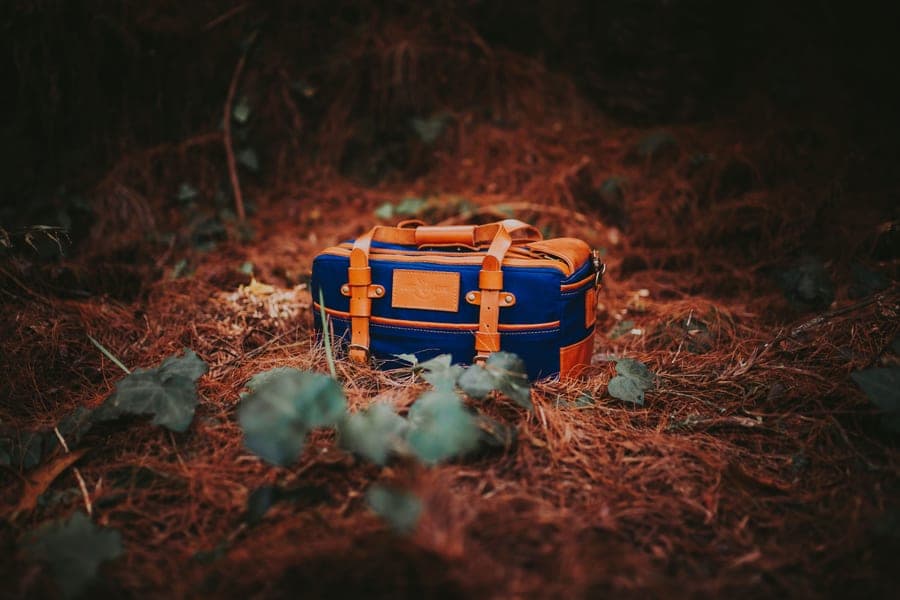 Canvas and leather duffel bag resting on pine needles in a dark forest