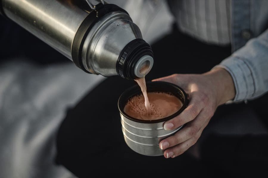 Hot cocoa poured from a steel vacuum bottle into its cup