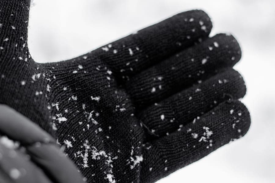 Black knit glove dusted with snowflakes, held open against a pale sky